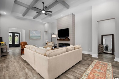 Living area with coffered ceiling, wood finished floors, a ceiling fan, a towering ceiling, and recessed lighting