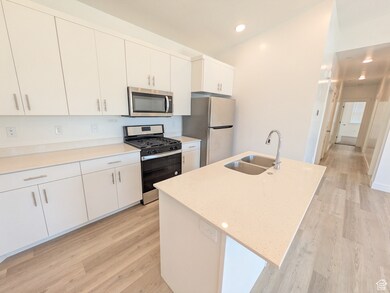 Kitchen with stainless steel appliances, light wood-style flooring, an island with sink, white cabinets, and recessed lighting