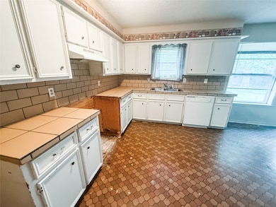 Kitchen with dishwasher, under cabinet range hood, backsplash, white cabinetry, and tile countertops
