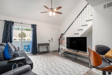 Living area with light wood-style floors, stairway, a ceiling fan, and high vaulted ceiling