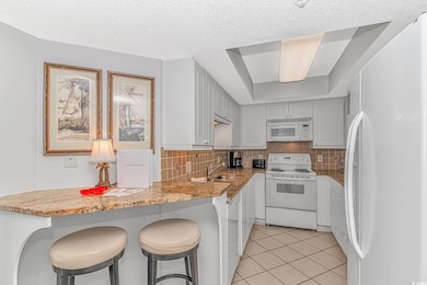 Kitchen featuring white appliances, a kitchen bar, backsplash, light tile patterned floors, and white cabinetry