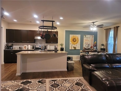 Kitchen with dark wood finished floors, backsplash, light stone counters, a kitchen island with sink, and recessed lighting