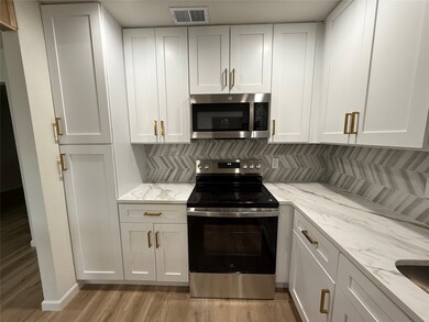 Kitchen with appliances with stainless steel finishes, white cabinetry, light wood-type flooring, and light stone countertops