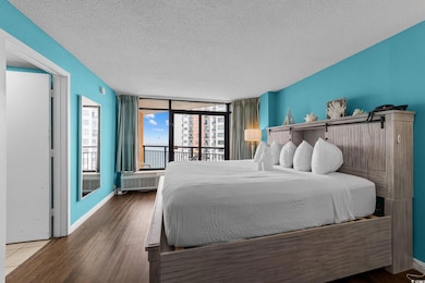 Bedroom featuring a textured ceiling, access to outside, wood finished floors, and baseboards