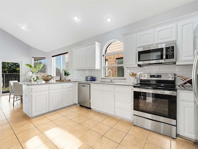 Kitchen with stainless steel appliances, a peninsula, light stone counters, white cabinetry, and vaulted ceiling
