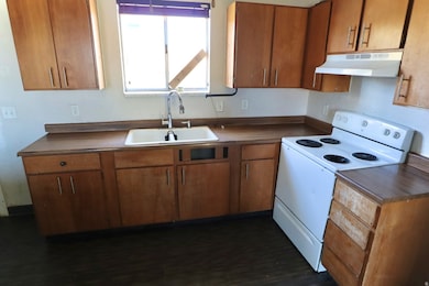Kitchen featuring electric stove, brown cabinets, under cabinet range hood, and dark countertops