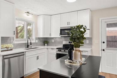 Kitchen featuring appliances with stainless steel finishes, light countertops, backsplash, and white cabinetry