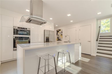 Kitchen with island exhaust hood, modern cabinets, appliances with stainless steel finishes, and white cabinetry