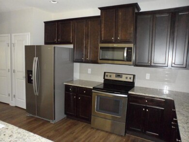 Kitchen with stainless steel appliances, dark wood-style floors, backsplash, light stone counters, and recessed lighting