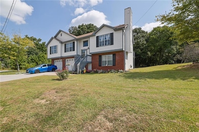 Raised ranch with a front yard, concrete driveway, brick siding, a chimney, and an attached garage