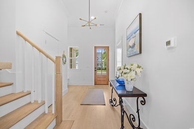 Foyer featuring stairway, a chandelier, light wood floors, a towering ceiling, and ornamental molding