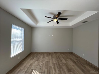 Empty room with a raised ceiling, wood finished floors, and ceiling fan