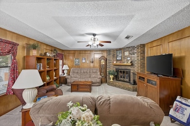 Living area with wooden walls, carpet flooring, a fireplace, ceiling fan, and a textured ceiling