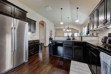 Kitchen with black appliances, a sink, arched walkways, a peninsula, and decorative backsplash