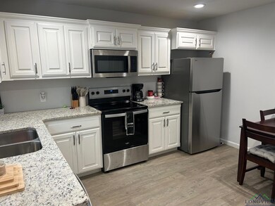 Kitchen with stainless steel appliances, white cabinets, light stone countertops, and light wood finished floors