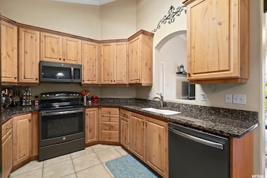 Kitchen featuring black range with electric cooktop, dishwasher, light tile patterned floors, dark stone counters, and ornamental molding