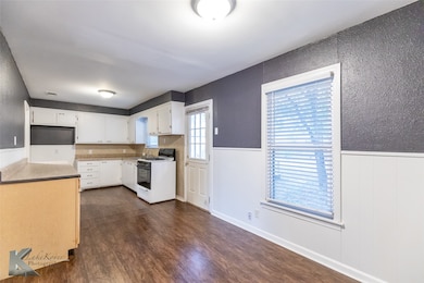 Kitchen featuring a wainscoted wall, gas range gas stove, dark wood finished floors, white cabinets, and a textured wall
