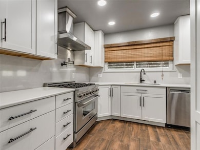 Kitchen with white cabinetry, dark wood finished floors, appliances with stainless steel finishes, wall chimney exhaust hood, and recessed lighting
