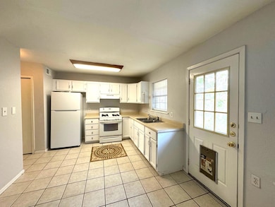 Kitchen with white cabinets, white appliances, light countertops, light tile patterned floors, and under cabinet range hood