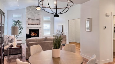 Dining area featuring wood finished floors, a stone fireplace, high vaulted ceiling, a chandelier, and recessed lighting