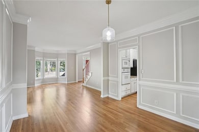 Spare room with stairway, light wood-type flooring, crown molding, and a decorative wall
