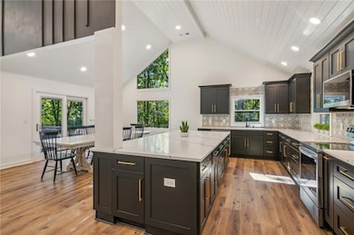 Kitchen featuring high vaulted ceiling, stainless steel appliances, light hardwood / wood-style flooring, and a kitchen island
