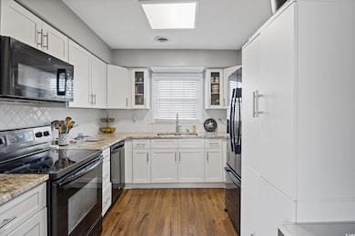 Kitchen featuring black appliances, dark wood finished floors, white cabinetry, and light stone counters