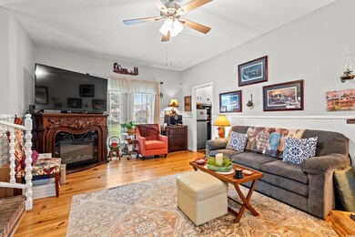 Living area featuring ceiling fan, wood finished floors, and a glass covered fireplace