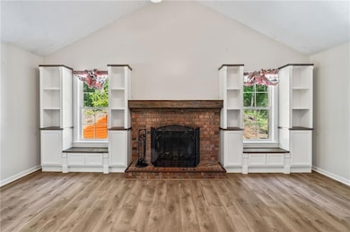 Unfurnished living room with light wood-style flooring, high vaulted ceiling, and a brick fireplace