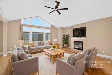 Living area featuring high vaulted ceiling, a tiled fireplace, ceiling fan, and light wood finished floors