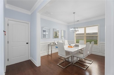 Dining space with a chandelier, dark wood-style flooring, wainscoting, a decorative wall, and crown molding