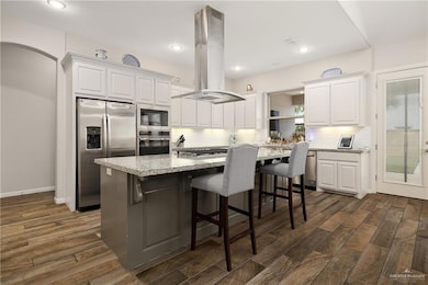 Kitchen with white cabinets, island exhaust hood, and stainless steel appliances