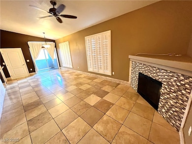Unfurnished living room featuring a fireplace, light tile patterned floors, a ceiling fan, and lofted ceiling