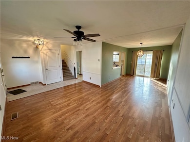 Unfurnished living room with light wood-style flooring, a chandelier, stairway, and ceiling fan