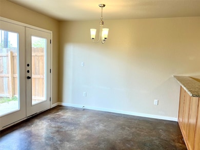 Unfurnished dining area featuring concrete flooring, french doors, a chandelier, and a textured wall