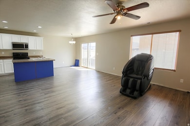 Kitchen featuring open floor plan, white cabinetry, black electric range oven, dark countertops, and a kitchen island with sink