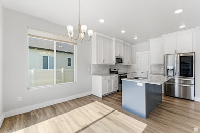Kitchen featuring stainless steel appliances, white cabinetry, pendant lighting, an island with sink, and a chandelier
