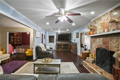 Living room featuring a tile fireplace, dark wood-type flooring, crown molding, ceiling fan, and recessed lighting