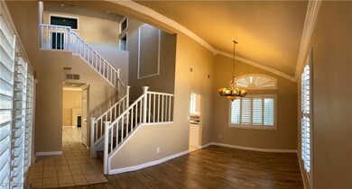 Stairway with ornamental molding, high vaulted ceiling, wood finished floors, and a chandelier