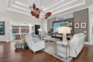 Living area featuring a tray ceiling, wood floors, decorative crown molding, arched walkways, and a ceiling fan and a new 85
