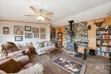 Living area with a wood stove, ceiling fan, a textured ceiling, wood walls, and wood finished floors