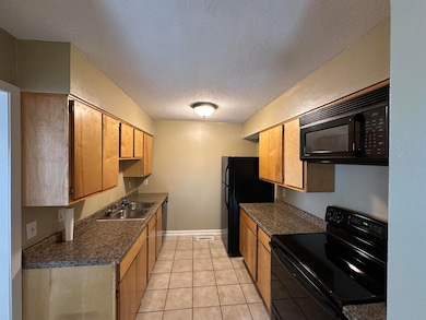 Kitchen featuring black appliances, a textured ceiling, dark countertops, and light tile patterned floors