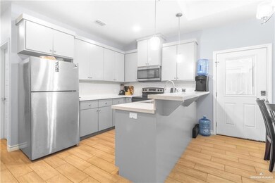 Kitchen featuring stainless steel appliances, a peninsula, light wood-style floors, hanging light fixtures, and light countertops