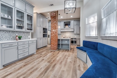 Kitchen with open shelves, gray cabinetry, decorative light fixtures, glass insert cabinets, and light wood finished floors