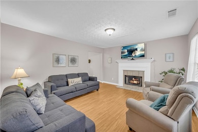 Living room with light wood-type flooring, a tiled fireplace, a textured ceiling, and baseboards