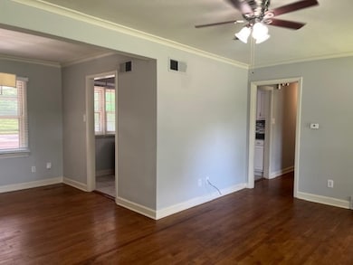 Empty room featuring plenty of natural light, dark wood-type flooring, a ceiling fan, crown molding, and baseboards
