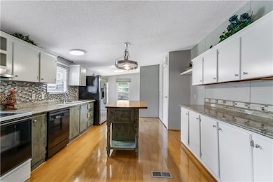Kitchen with black dishwasher, electric range, a sink, stainless steel fridge with ice dispenser, and light wood-style flooring