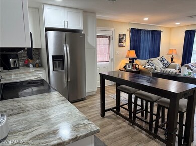Kitchen with white cabinets, stainless steel fridge with ice dispenser, backsplash, light stone countertops, and recessed lighting