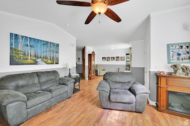 Living area with ornamental molding, a ceiling fan, light wood-style flooring, vaulted ceiling, and a glass covered fireplace