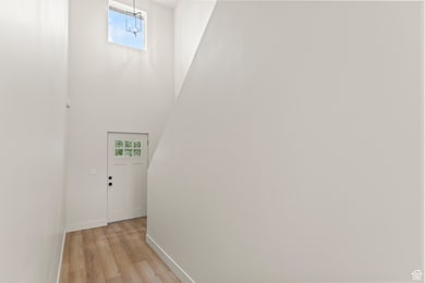 Corridor with healthy amount of natural light, a towering ceiling, and light wood finished floors